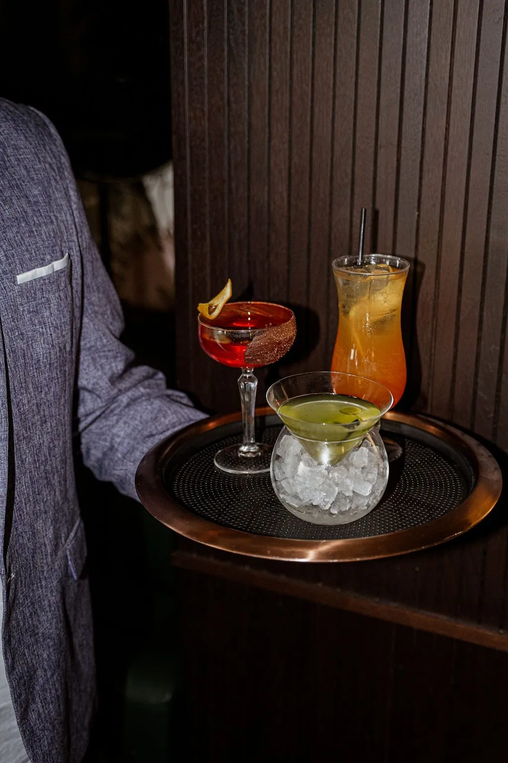 A server carrying a tray of three cocktails