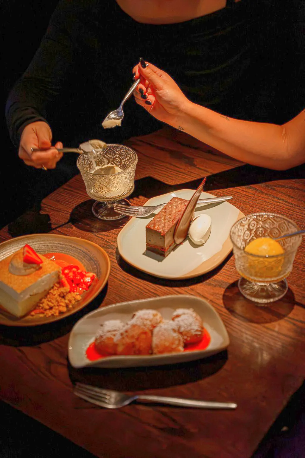 Desserts on a wood table: tres leches cheesecake, chocolate cake, guava beignets and ice cream