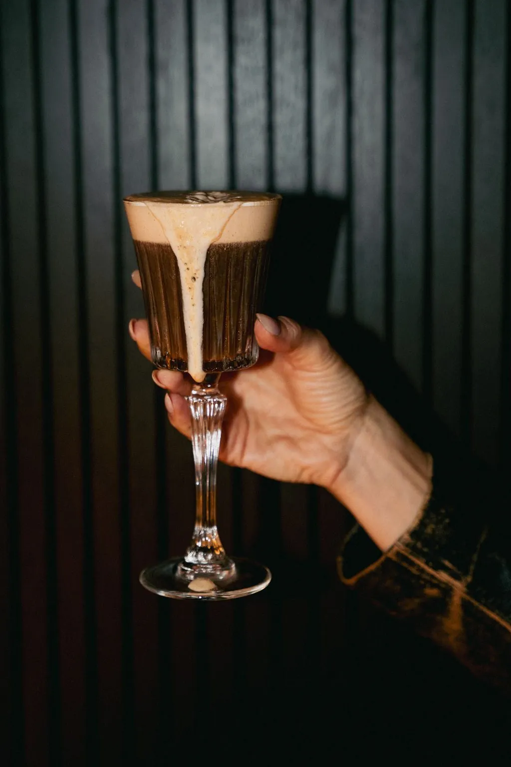 A dark cocktail with a pale foam head in a stemmed glass