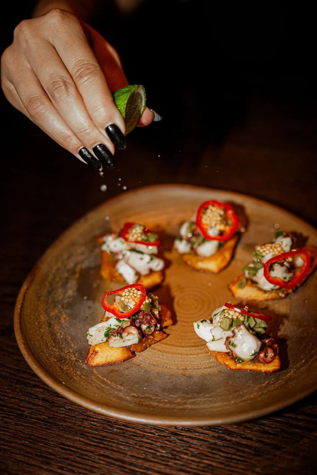 Octopus tostones on a stoneware plate, a hand squeezing lime over them