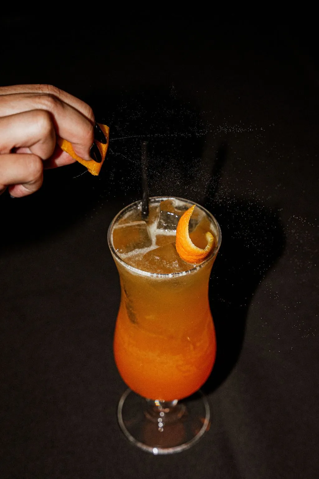 An orange peel going onto a tall amber cocktail