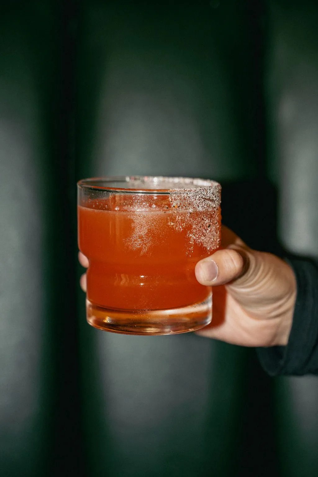 A salt-rimmed red cocktail held against a dark green wall