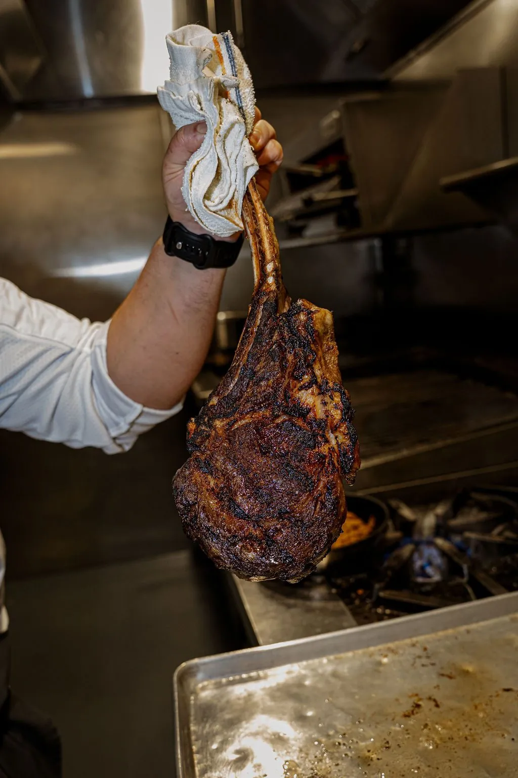 A cook holding up a seared tomahawk in the kitchen