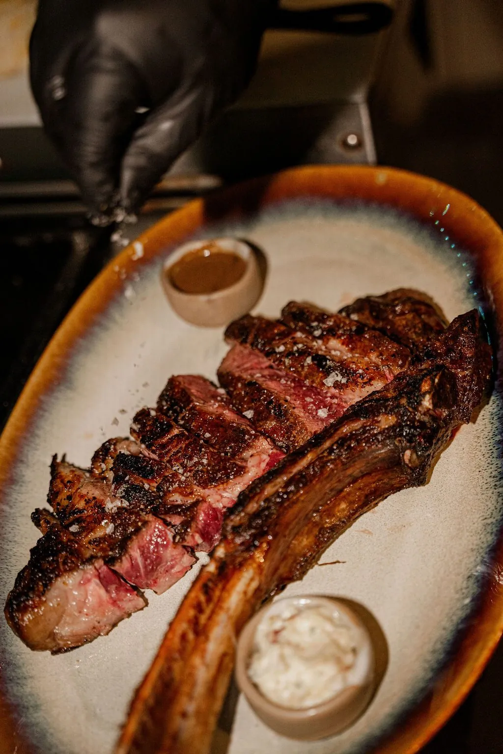 A sliced tomahawk on a platter with two sauces